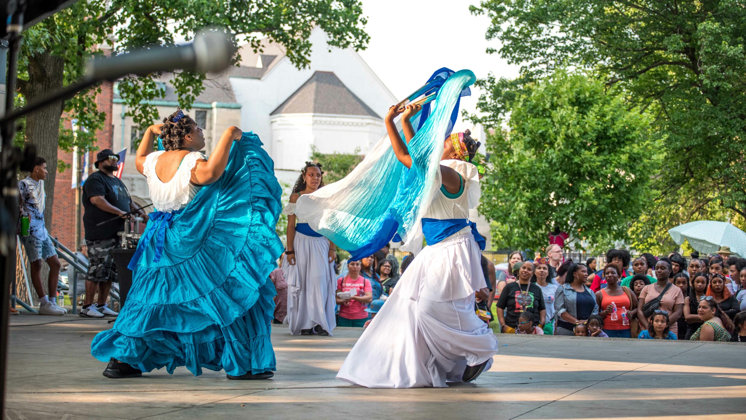 Women dancing in colorful blue outfits on stage at Bronson Park