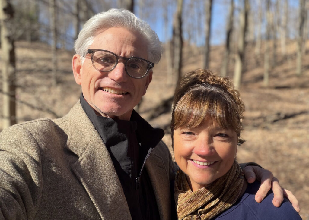 Photo of Ken and Dana smiling in front of a wooded background